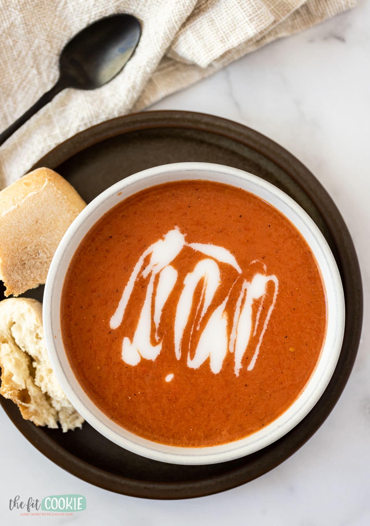 overhead photo of dairy free tomato soup with a coconut milk drizzle in a white bowl. 