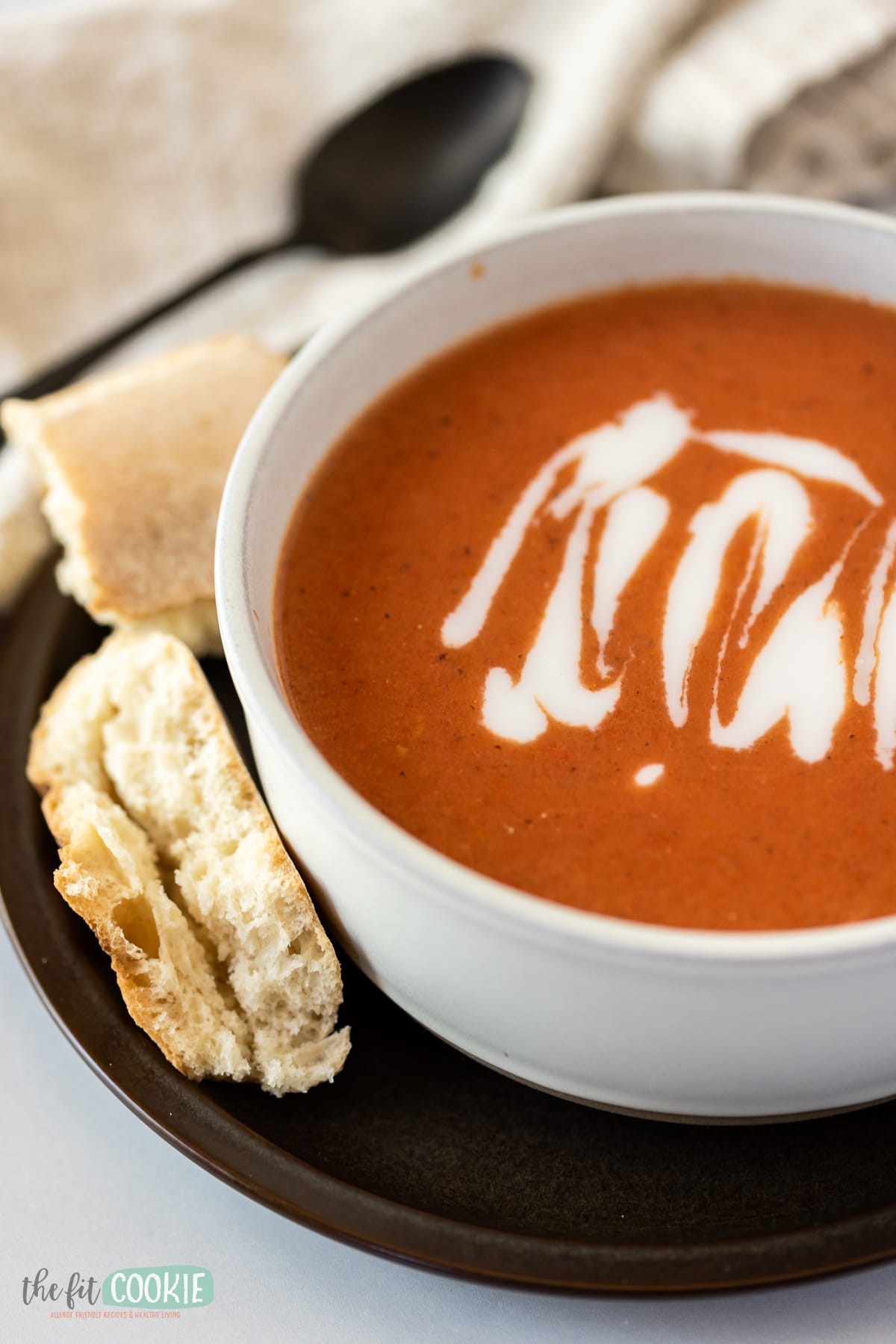 close up photo of tomato soup in a white bowl with coconut cream drizzle on top. 