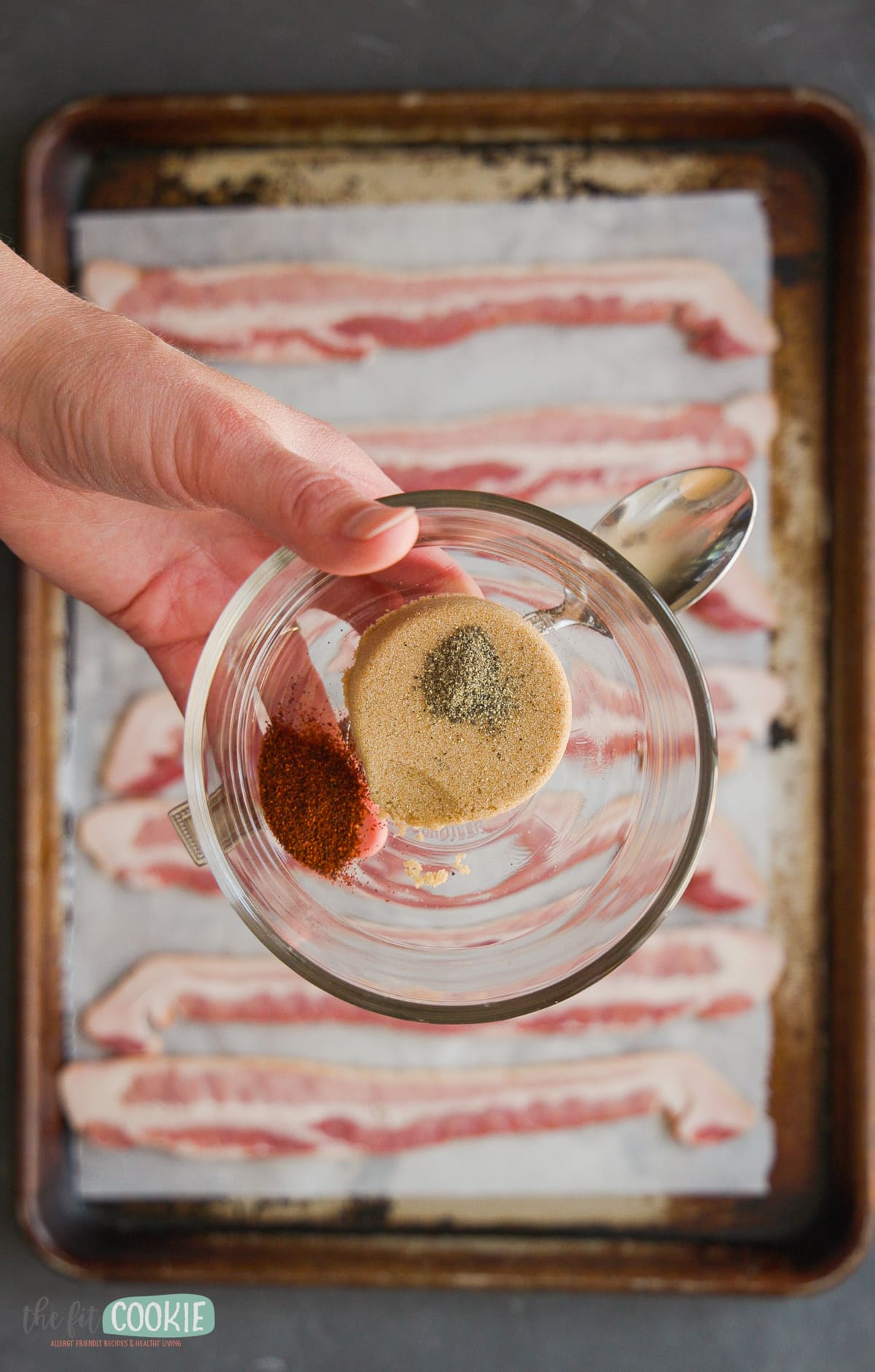overhead photo of hand holding glass dish with spices and brown sugar.