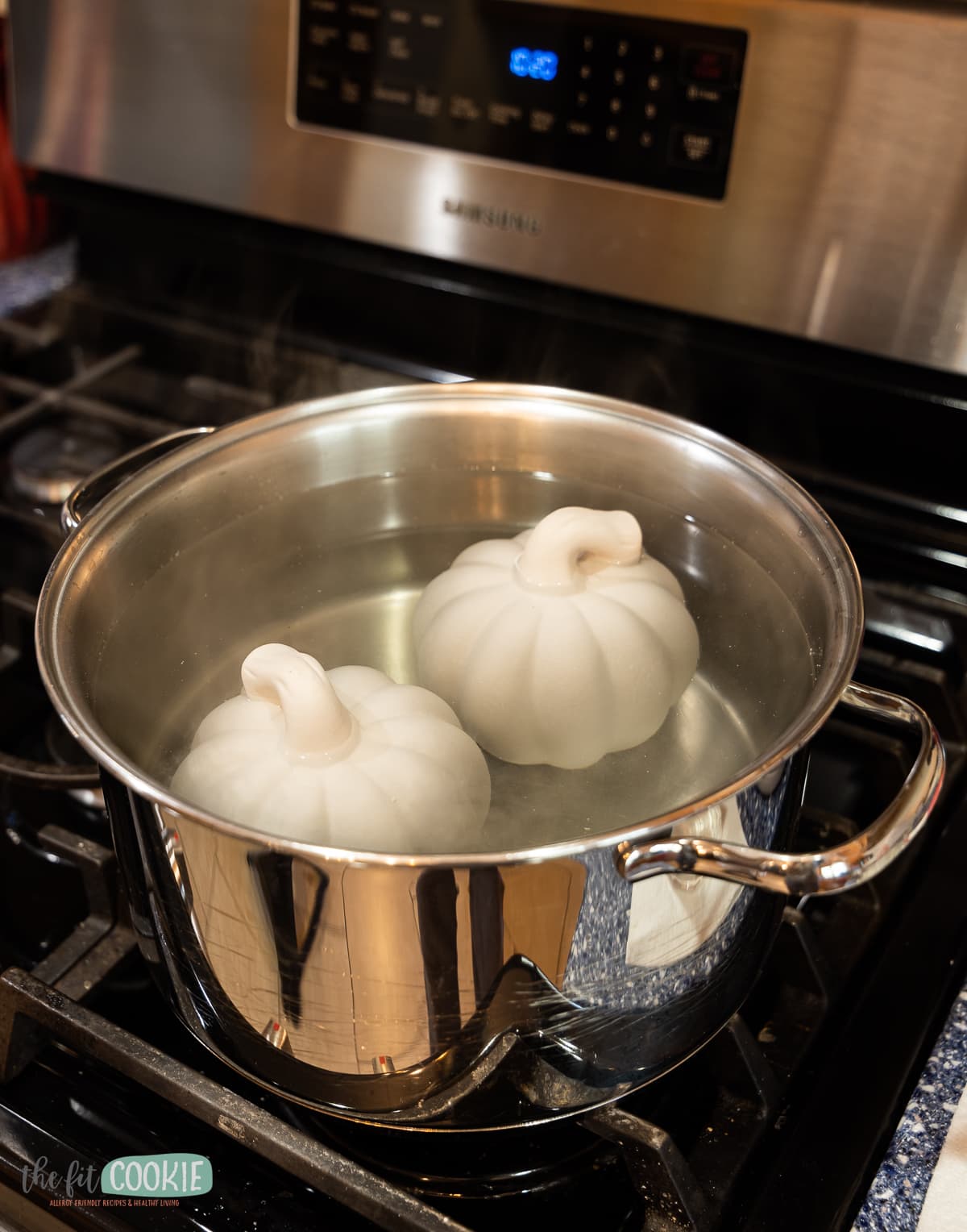 photo of a pot of water on the stove with 2 ceramic pumpkins in the pot. 