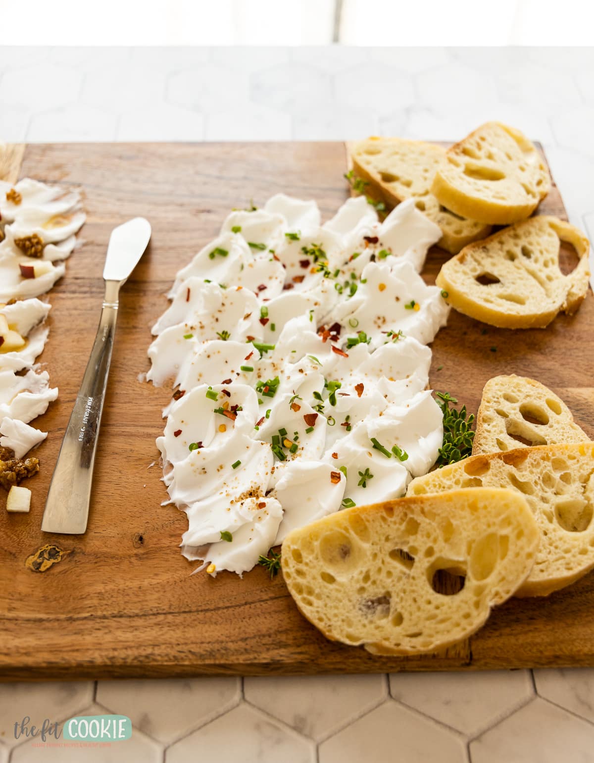 close up photo of a savory cream cheese spread on a wood board with slices of italian bread. 
