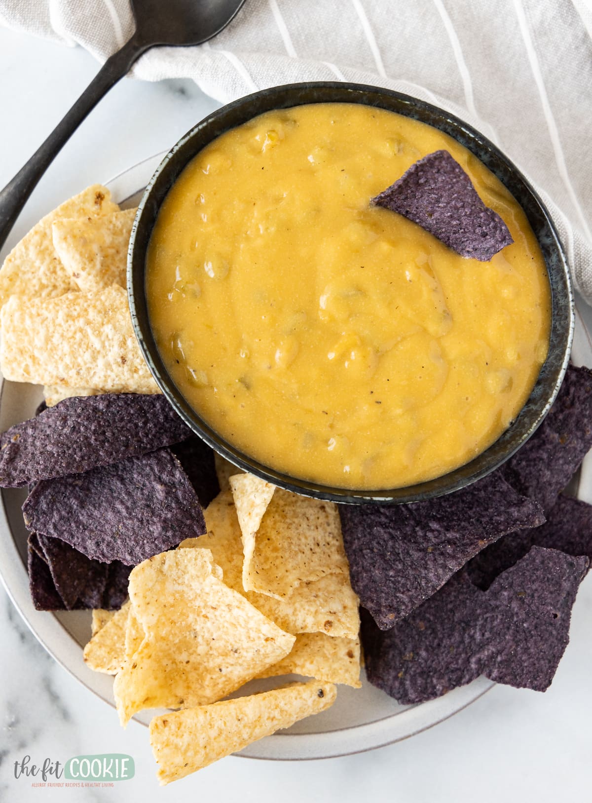 overhead photo of a bowl of queso surrounded by white and blue tortilla chips. 