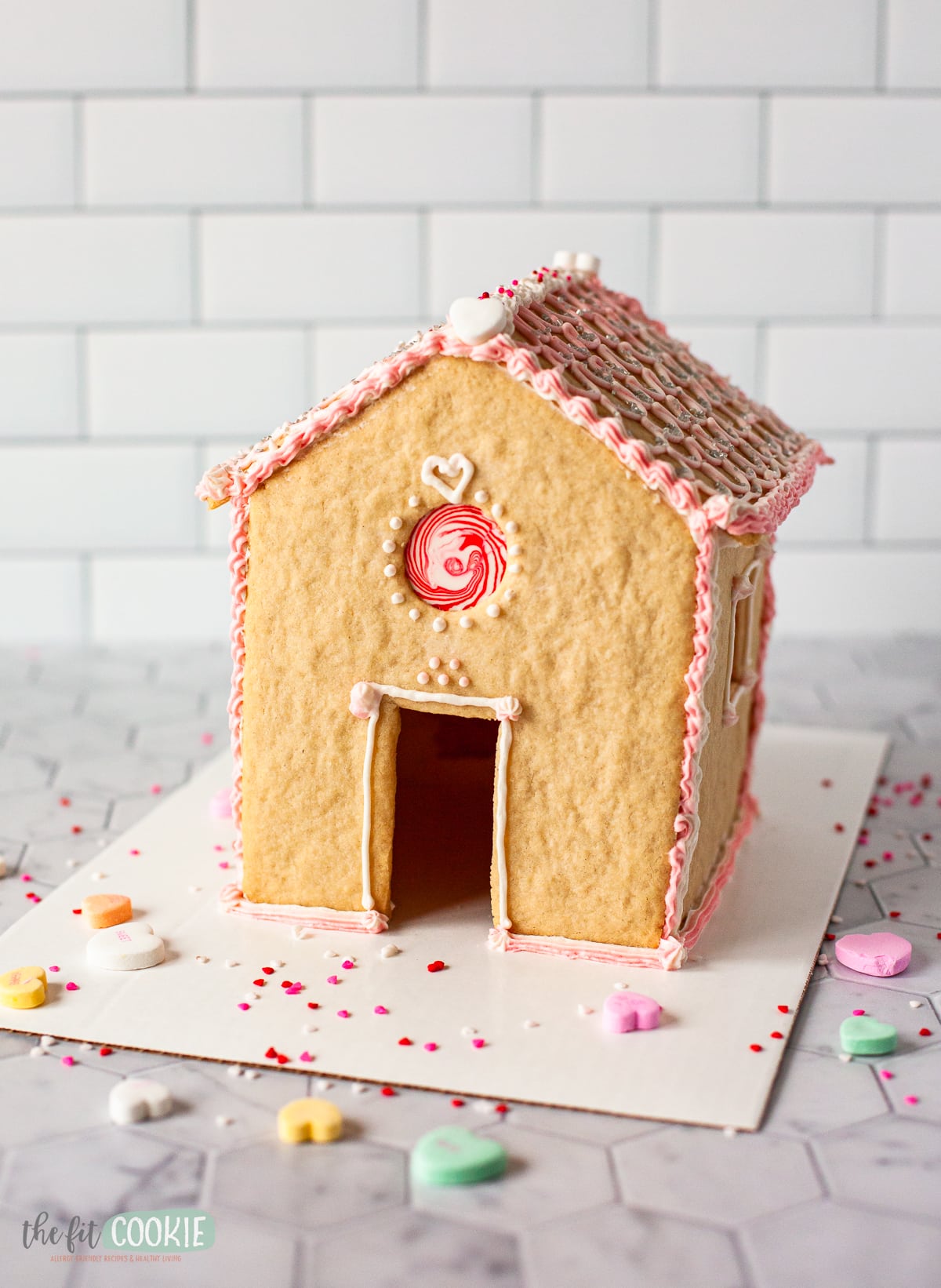 photo of a valentine decorated sugar cookie house on a white cake board. 