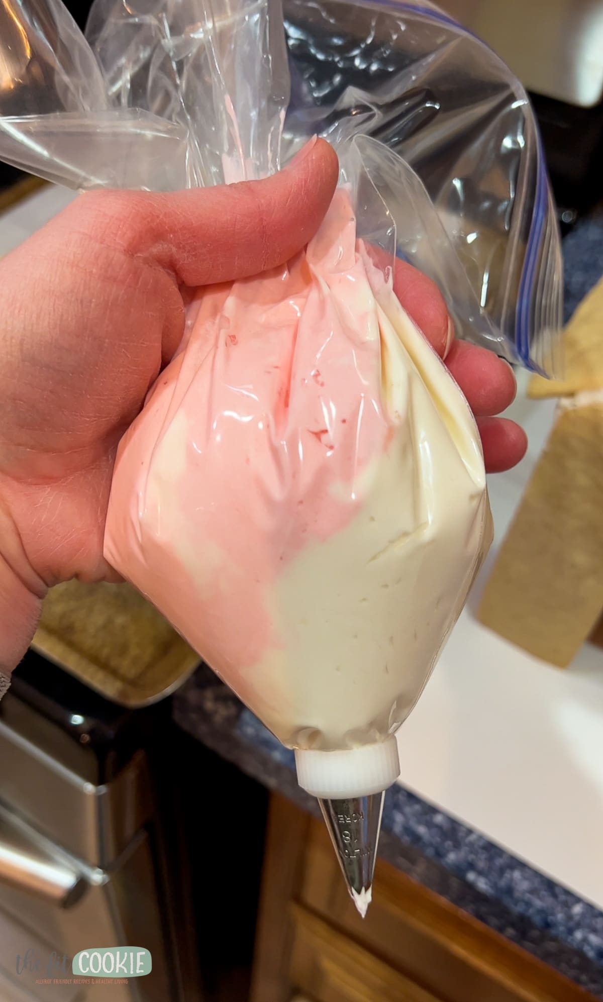 Hand holding a plastic bag with pink and white frosting inside for piping. 