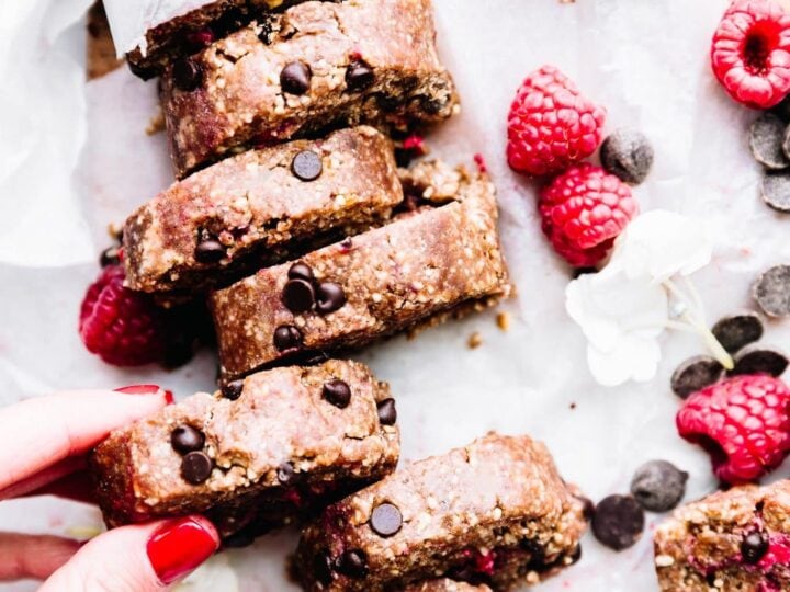 A person is holding a stack of granola bars with raspberries.