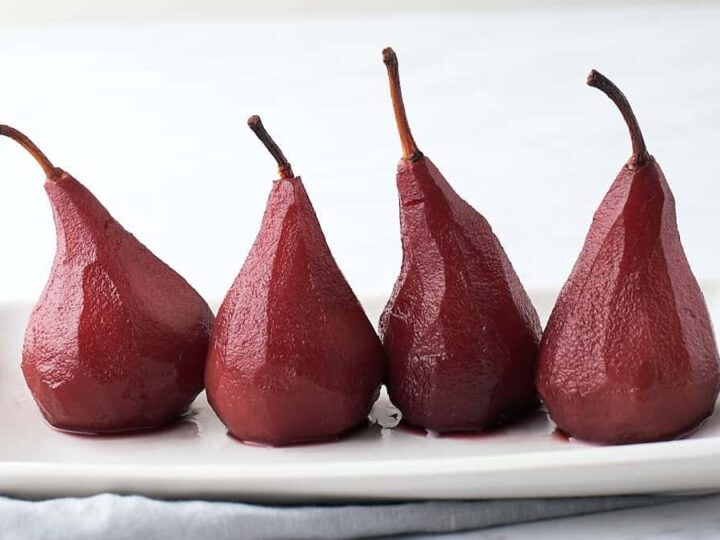 Four red pears on a white plate.