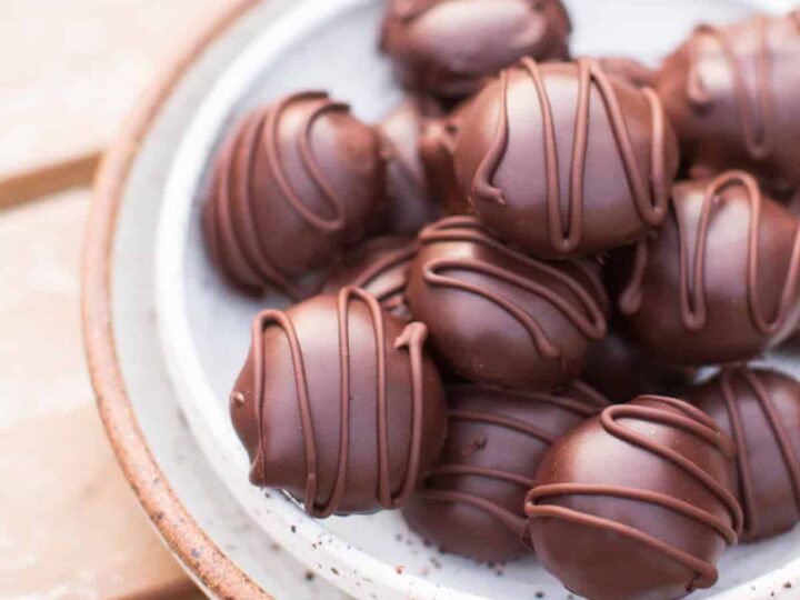 Chocolate truffles in a white bowl on a wooden table.