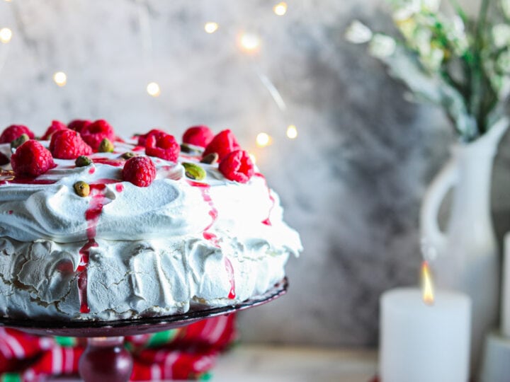 A christmas pavlova with raspberries on a cake stand.