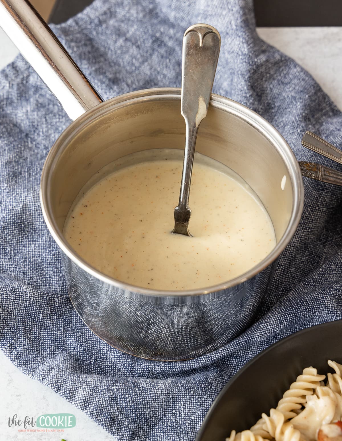 small saucepan filled with dairy free alfredo sauce on a blue napkin. 