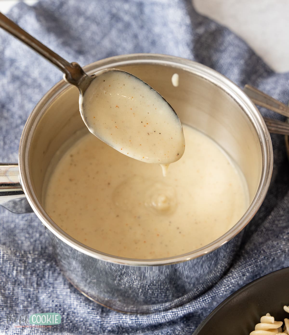 photo of dairy free alfredo sauce in a small saucepan with a spoon. 