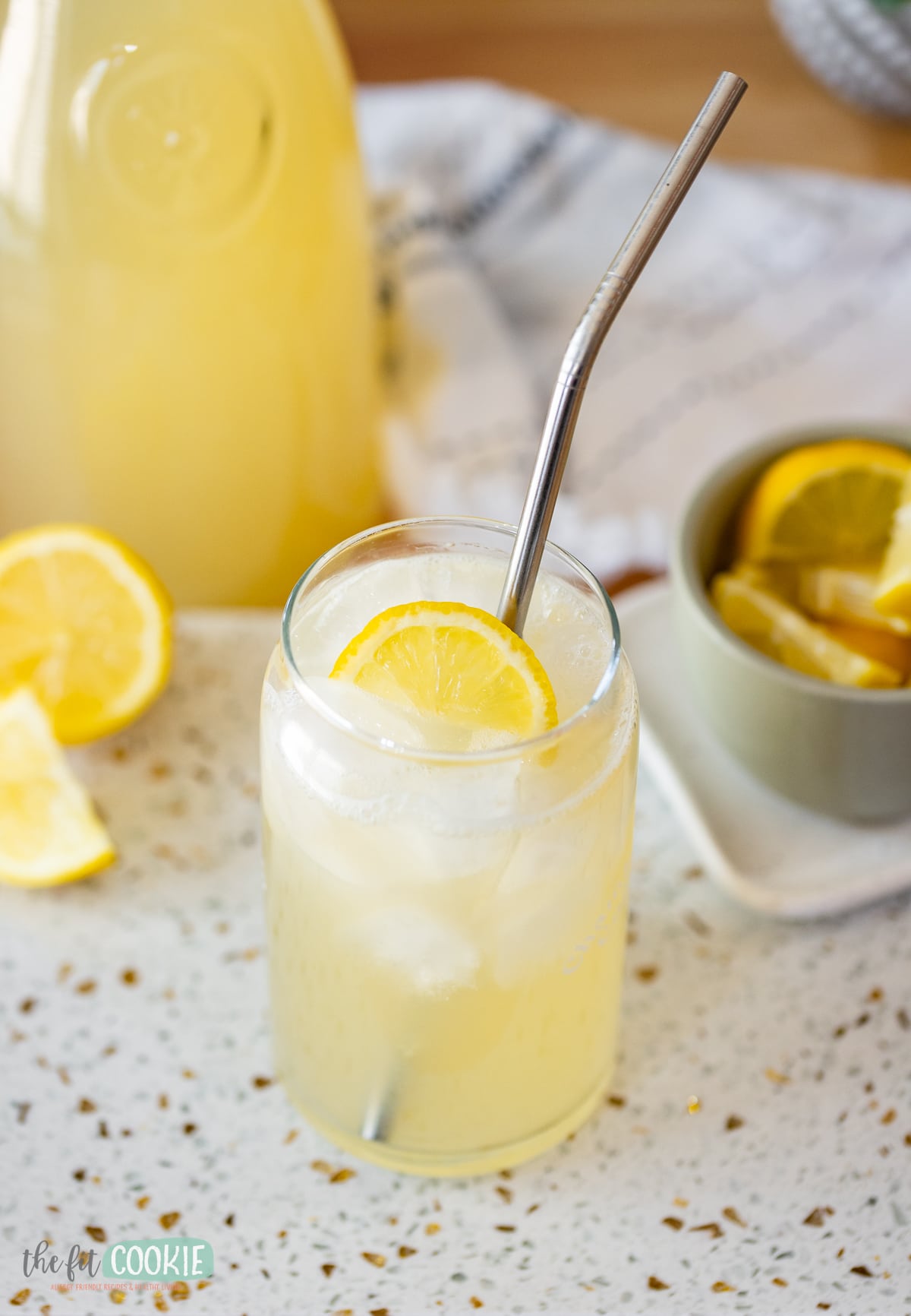 close up photo of a glass can-shaped jar filled with ice and lemonade with a metal straw. 