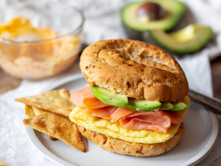 A breakfast sandwich with salmon and avocado on a bagel.