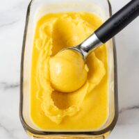 A bowl of mango sorbet with a spoon in it.