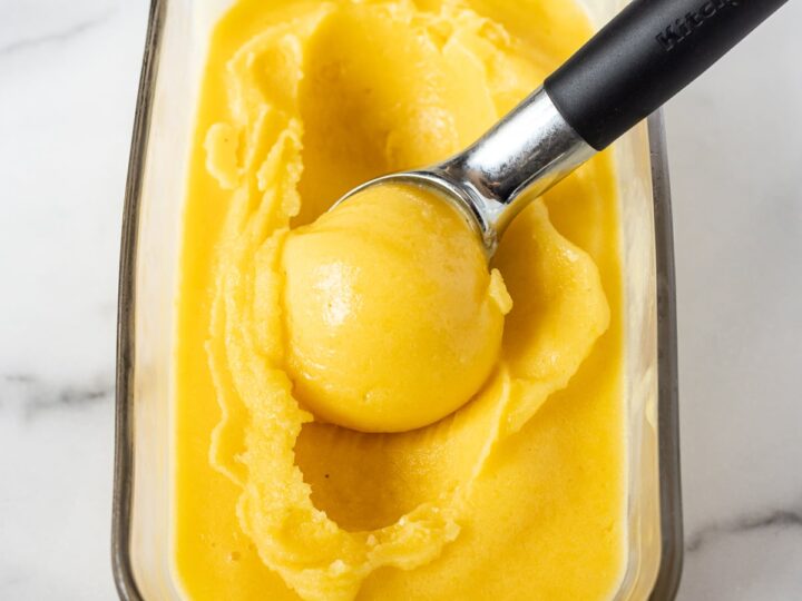 A bowl of mango sorbet with a spoon in it.