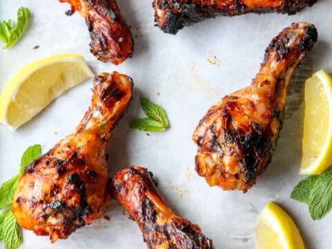 Grilled chicken wings on a white plate with lemon wedges.