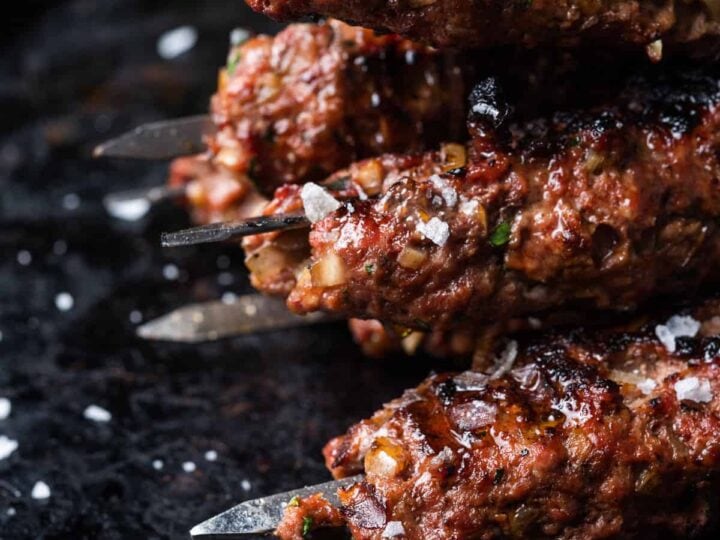 Kebabs on skewers on a black plate.