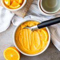 A bowl of orange sherbet with a spoon next to it.