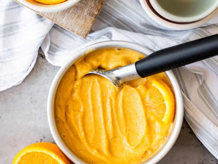 A bowl of orange sherbet with a spoon next to it.