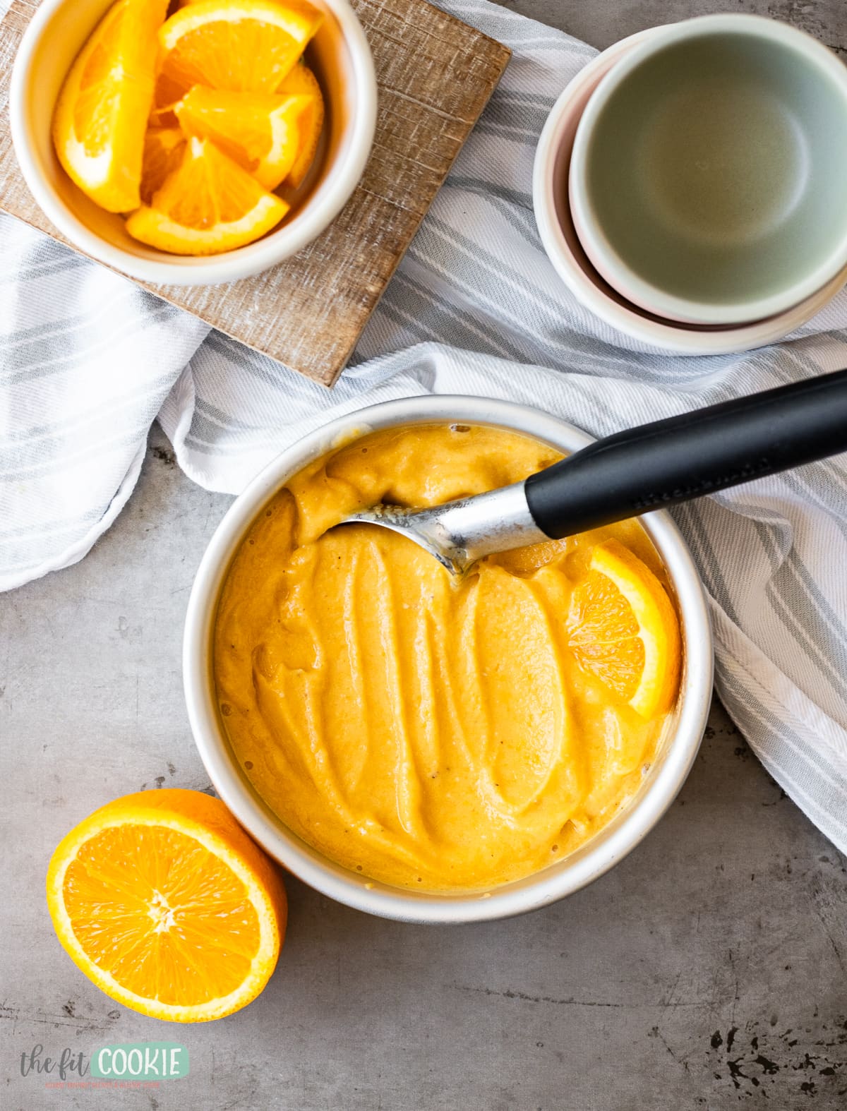 A bowl of orange sherbet with a spoon next to it.