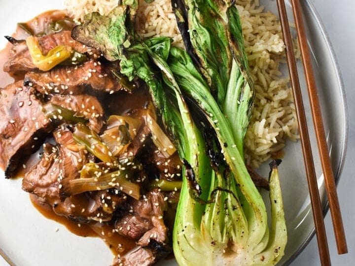 A plate with beef, broccoli and chopsticks.