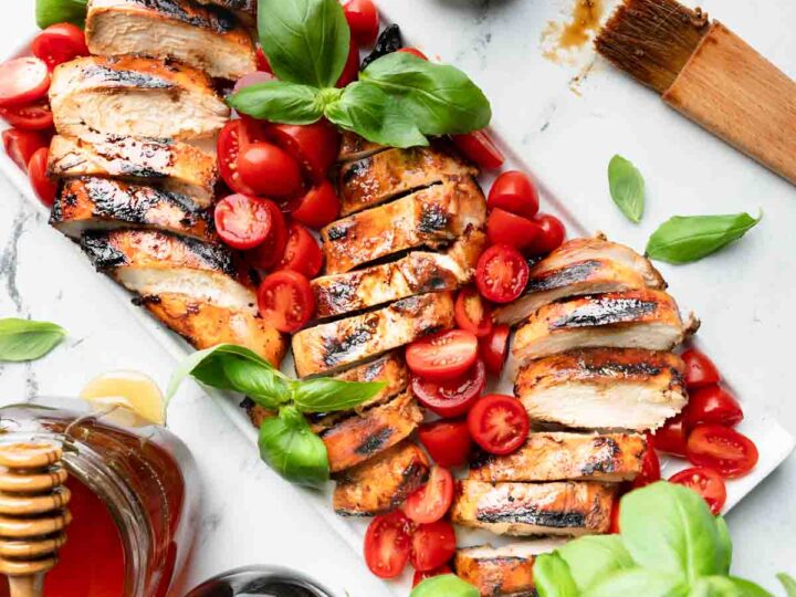 Grilled chicken with tomatoes and herbs on a white plate.