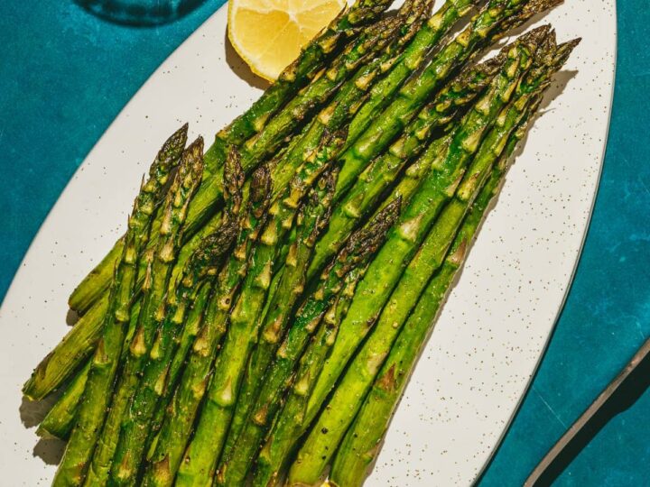 A plate of asparagus with lemon wedges on it.