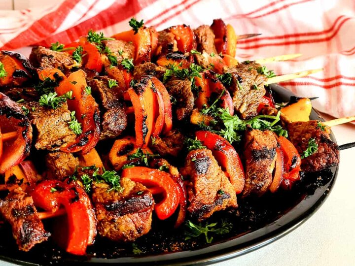 Grilled meat skewers on a black plate.