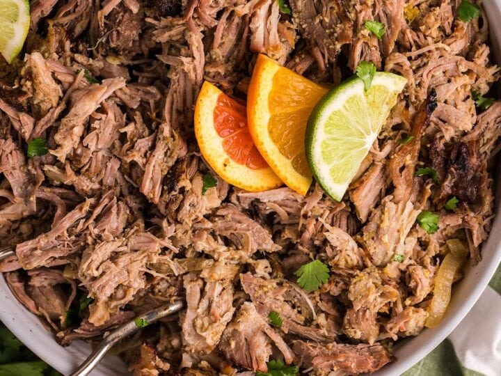 A plate of pulled pork with orange slices and limes.