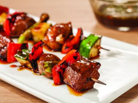 Meat skewers with vegetables and sauce on a white plate.