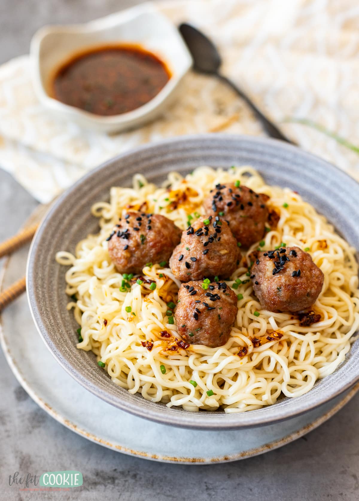 pork meatballs with black sesame seeds on top of noodles in a gray bowl. 