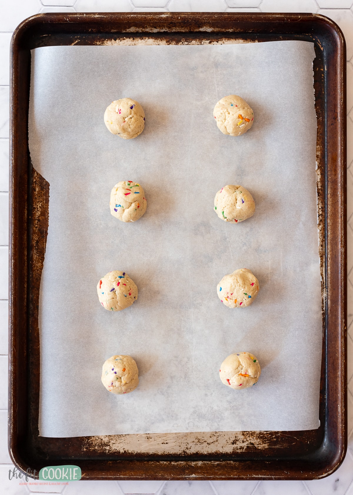 overhead photo of funfetti cookie dough balls on a parchment paper lined cookie sheet. 