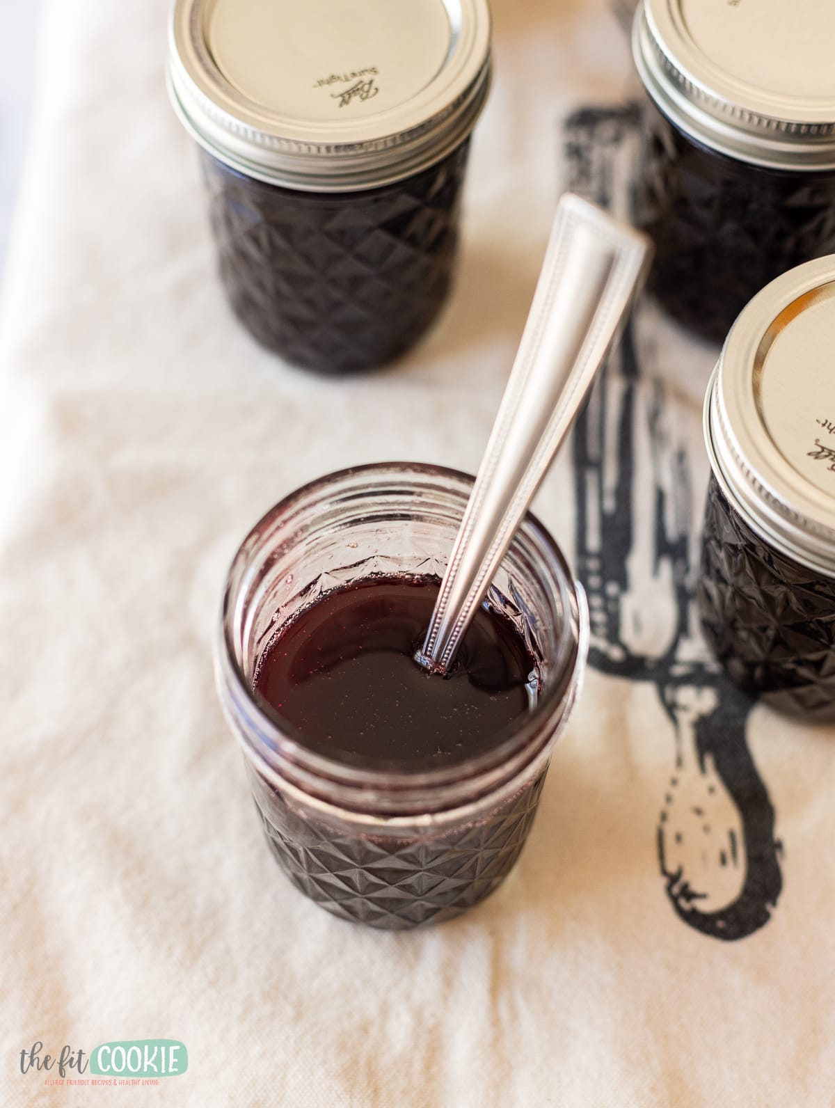 Jars of chokecherry syrup with a spoon in them.