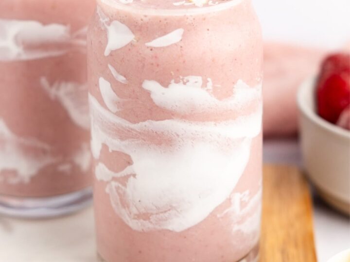 Two glasses of strawberry smoothie with whipped cream and strawberries.