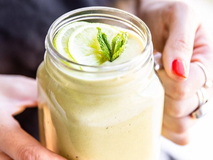 A woman holding a jar with a lime and mint in it.