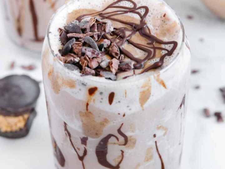 A chocolate peanut butter milkshake in a glass surrounded by peanut butter cups.
