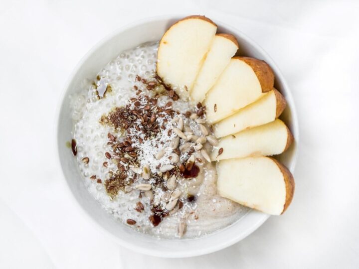 A bowl of oatmeal topped with apples and nuts.