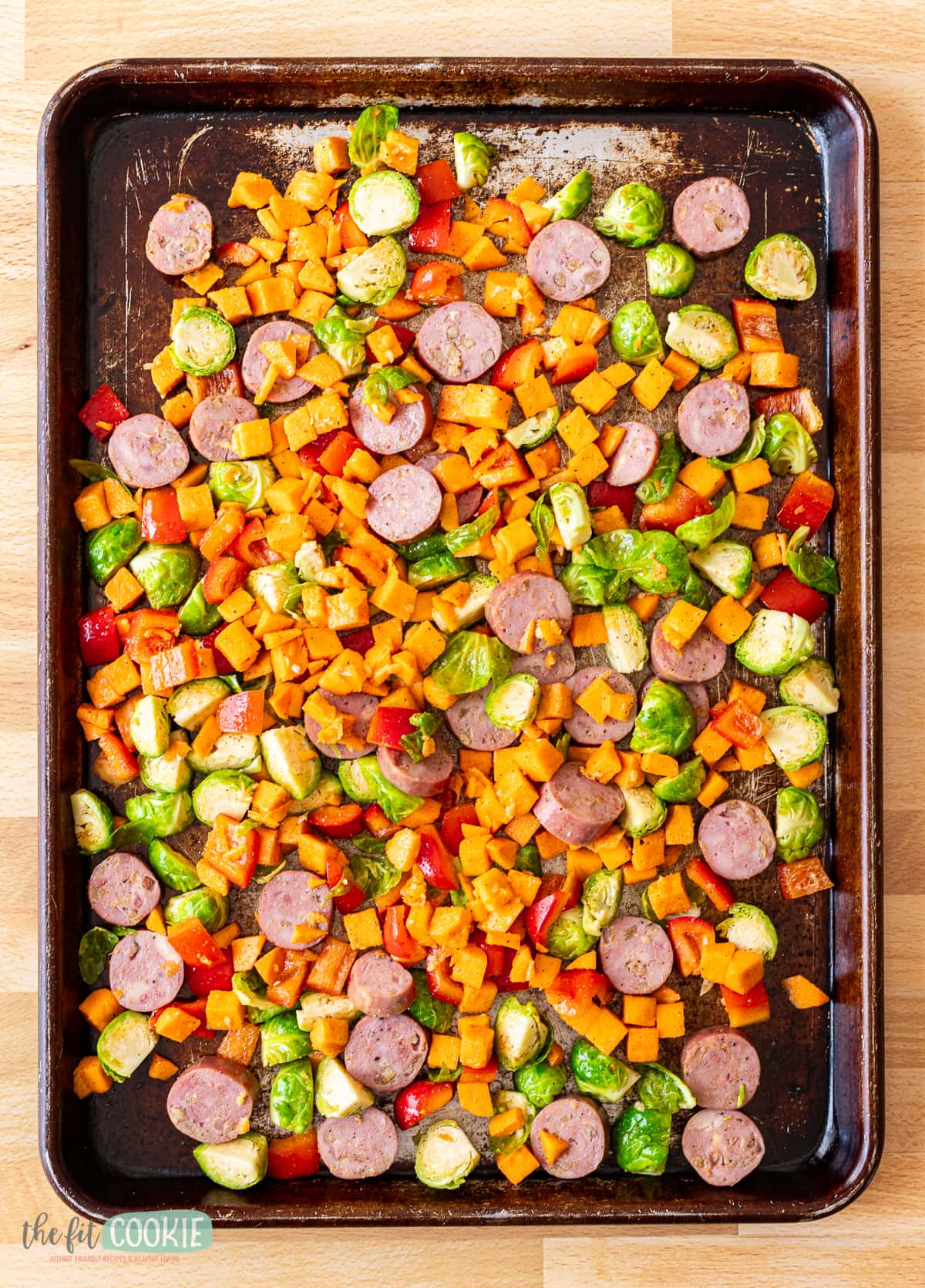 Overhead photo of a sheet pan with sausage and uncooked veggies on it ready to go to the oven. 
