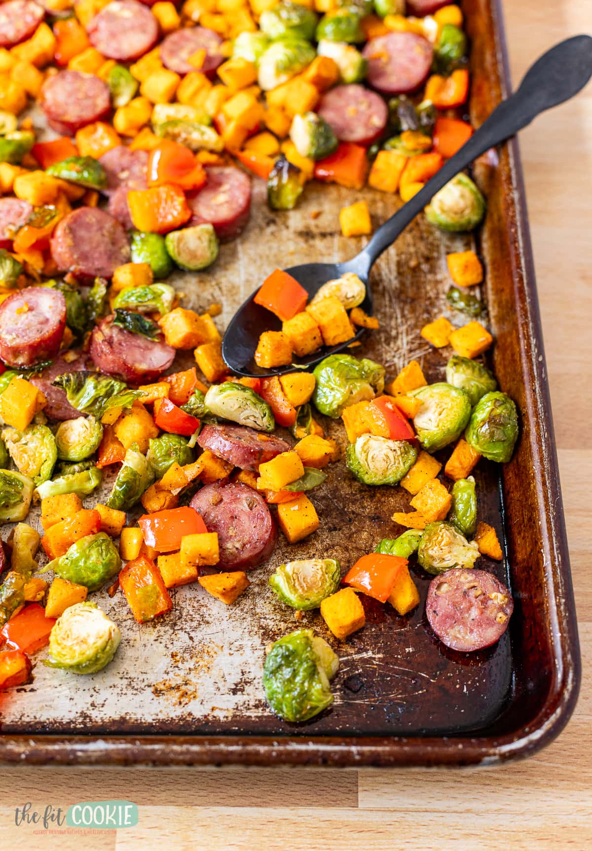 Close up photo of sausage and veggie sheet pan dinner with a black spoon in it. 