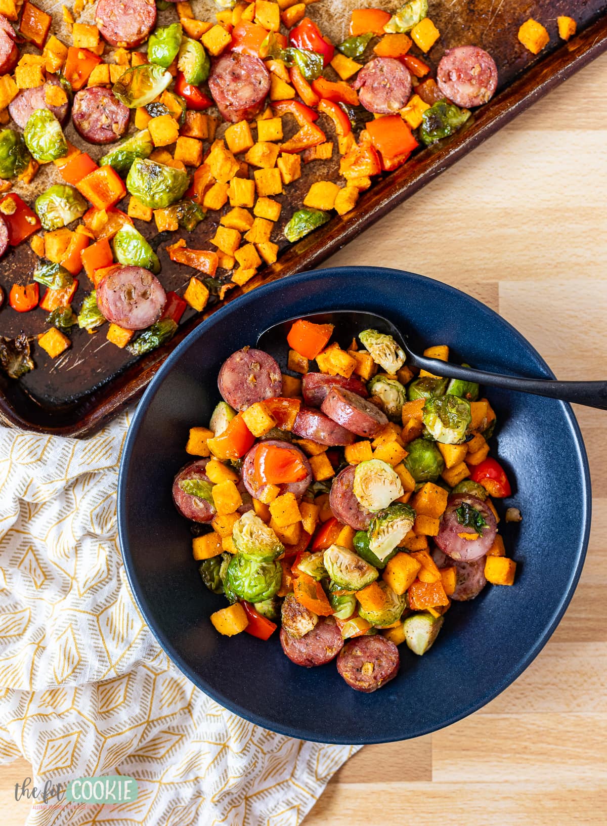 Overhead photo of sheet pan sausage and veggies in a dark blue bowl. 