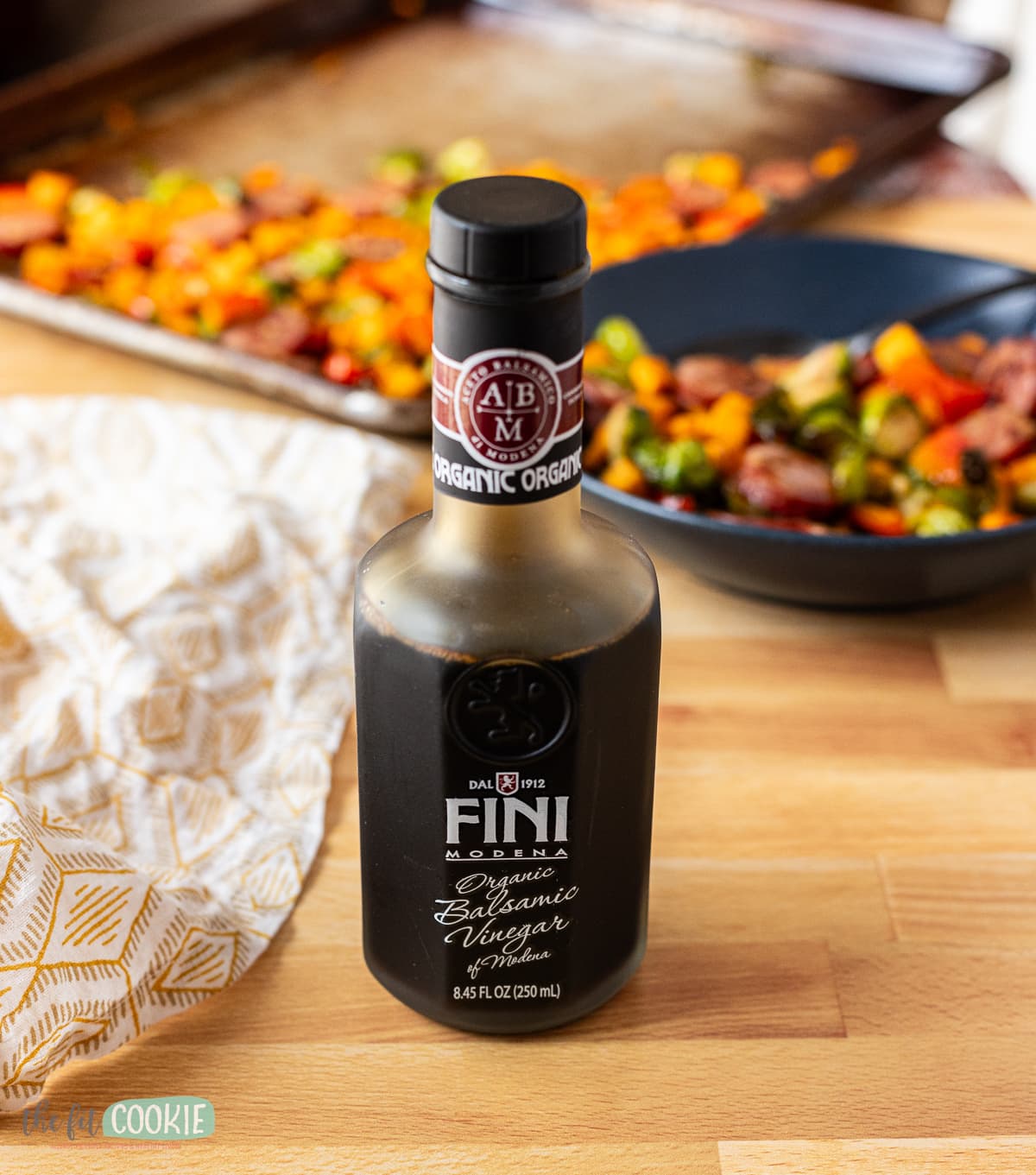 A sheet pan with sausage and veggies next to a bottle of fini balsamic vinegar. 