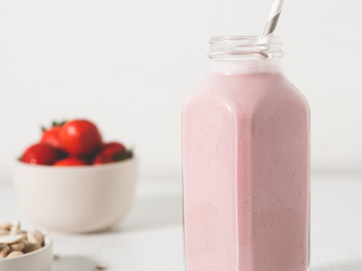 A pink smoothie with strawberries and almonds on a white background.