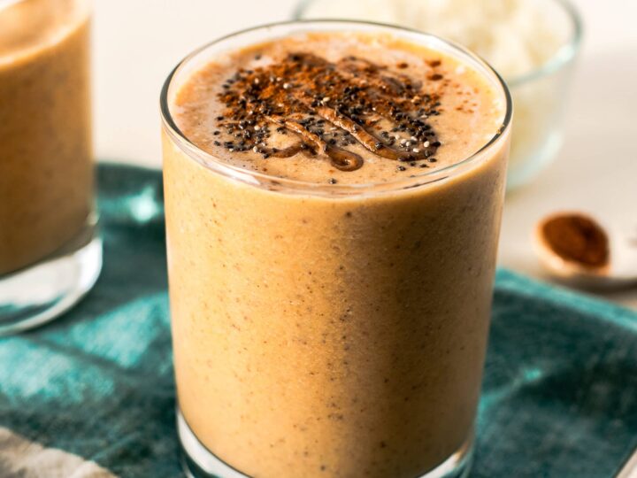 Two glasses of dessert smoothie with cinnamon and nutmeg on a table.