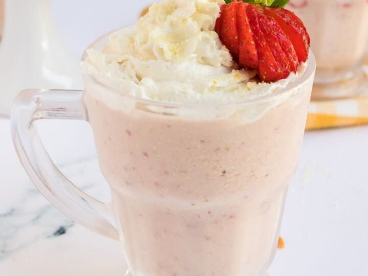 A strawberry milkshake with whipped cream and strawberries.