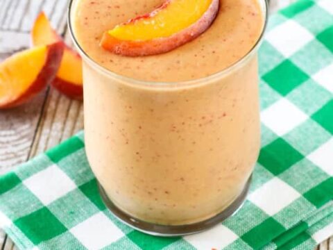 Peach smoothie in a glass on a checkered napkin.