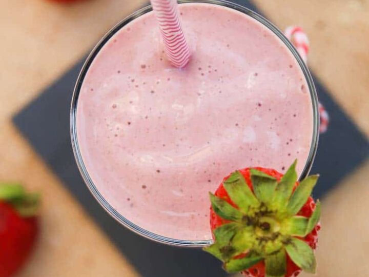 A strawberry smoothie in a glass with a straw.