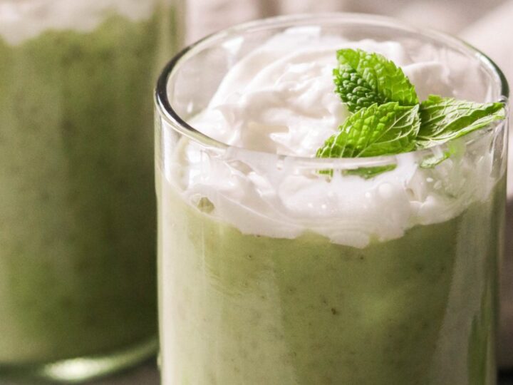 Two glasses of green smoothie with whipped cream and mint leaves.
