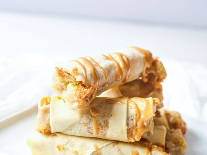 A plate with a stack of air fried banana peanut butter spring rolls.