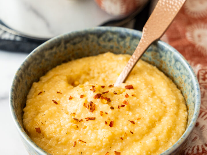 A bowl of cheese grits with a spoon next to it.
