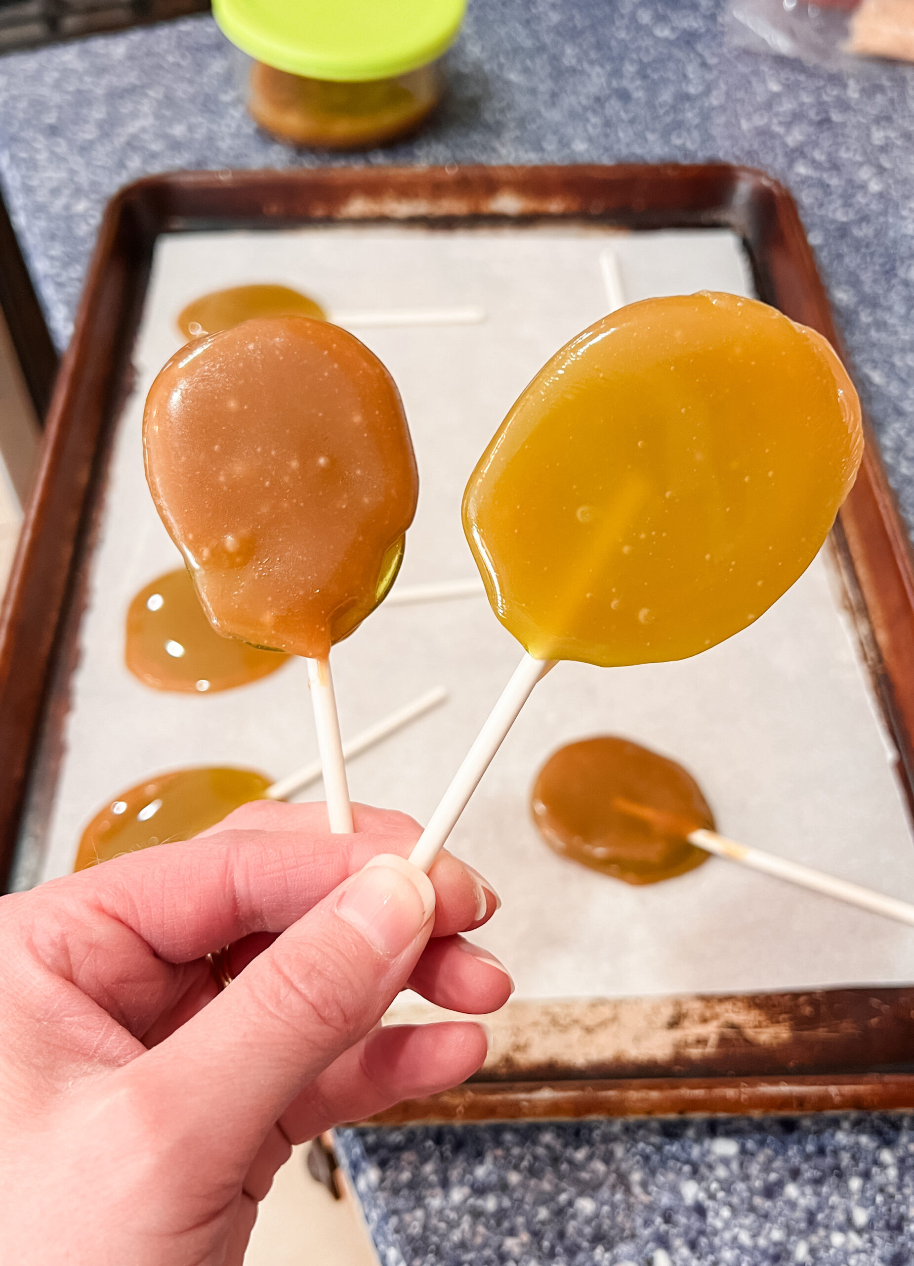 A person holding two caramel apple suckers on a baking sheet.