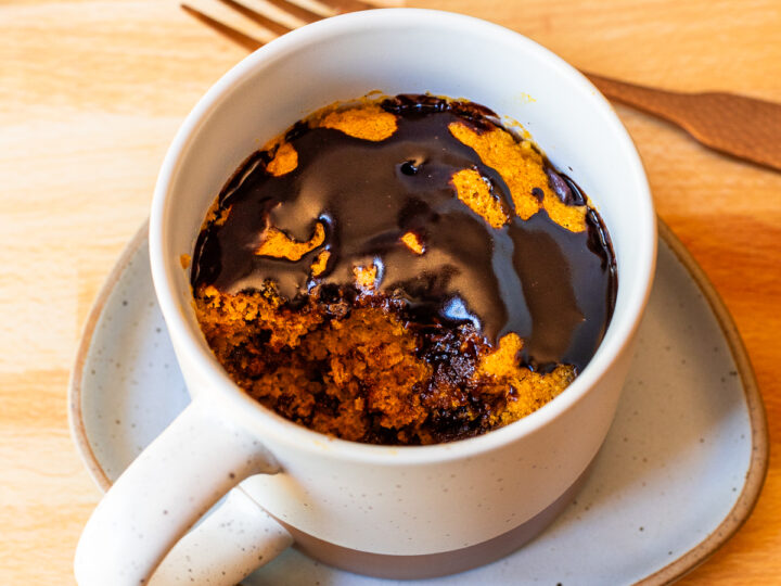A pumpkin mug cake with a fork on top, served in a mug.